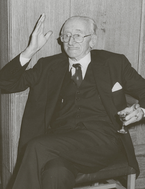 Vana prillidega mees istumas toolis ühes kões pokaal, teist kätt üleval hoidmas